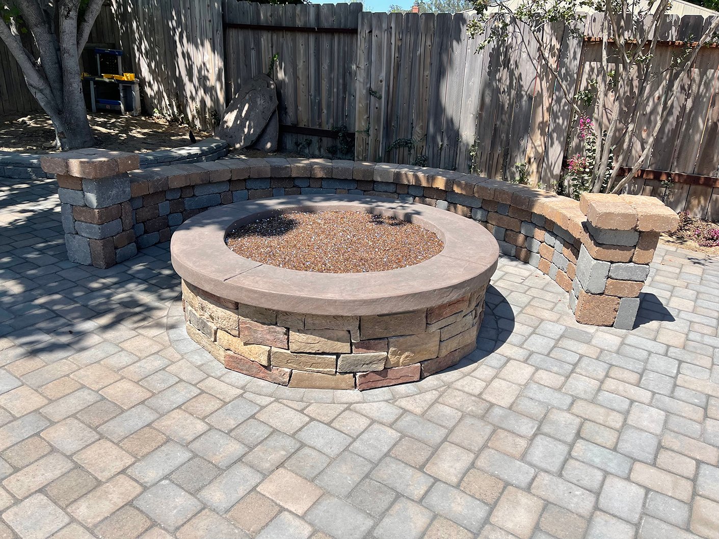 Custom paver patio with a built-in gas fire pit and seating wall in a Central Coast backyard